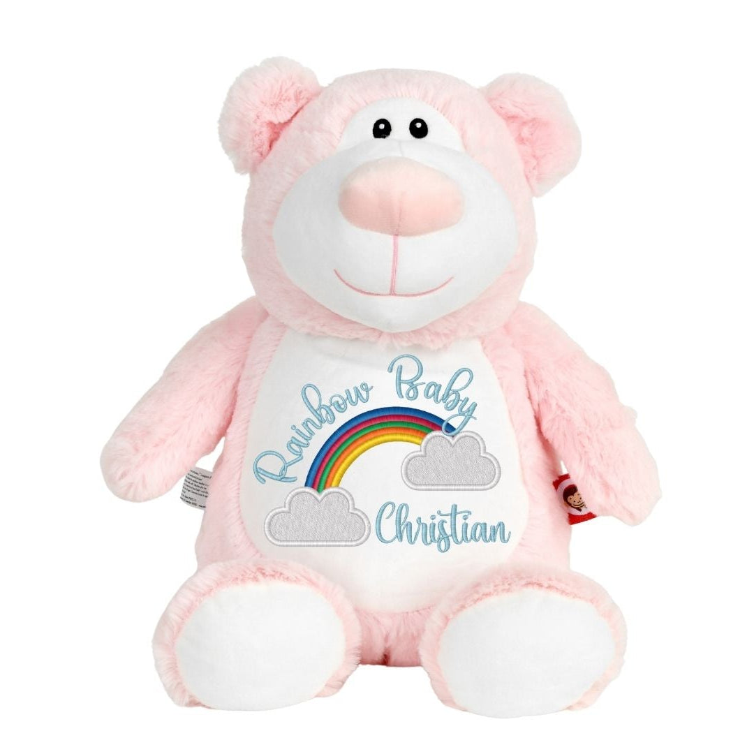 A pink plush teddy bear with a white belly patch that reads 'Rainbow Baby Christian' with a small rainbow and clouds, shown on a plain white background.